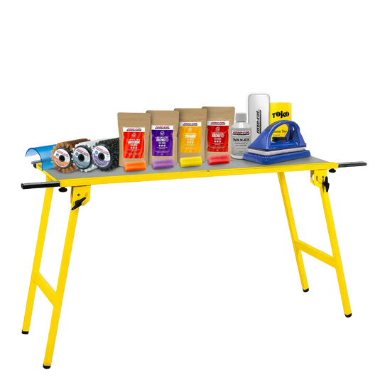 Gelber Klapptisch mit verschiedenen Wachsprodukten, Bürsten und einem Wachsbügeleisen für Ski- oder Snowboardpflege.