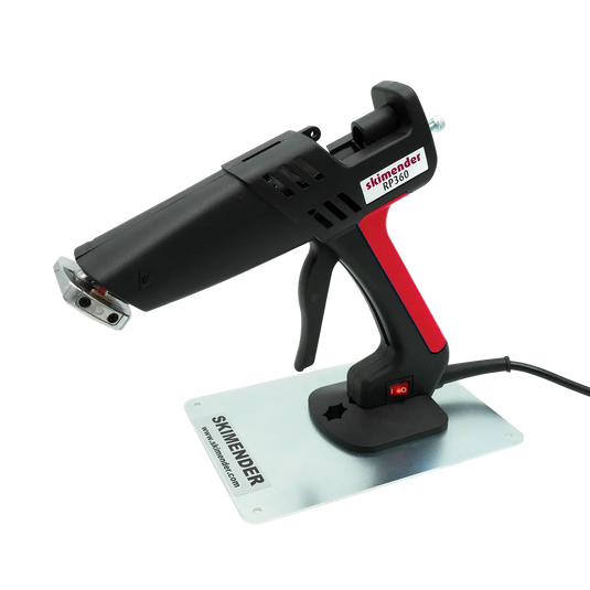 Heißklebepistole mit schwarzem und rotem Griff auf Metallplatte mit der Aufschrift 'SKIMENDER'