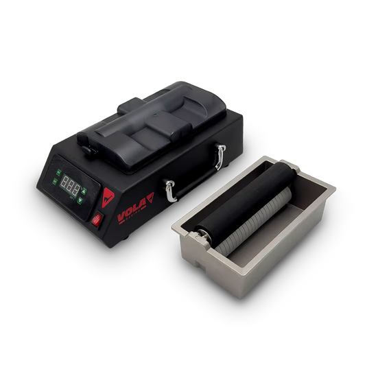 Wachsmaschine in schwarz mit rotem VOLA Logo und Digitalanzeige. Wachsschale in grau daneben. Darin sind zwei Walzen übereinander angeordnet.